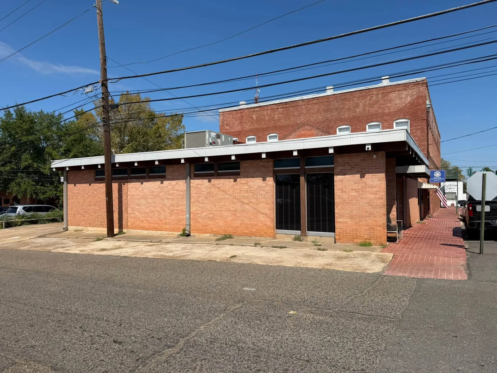 Brick building beside a sidewalk, with a low roof and overhead utility lines.