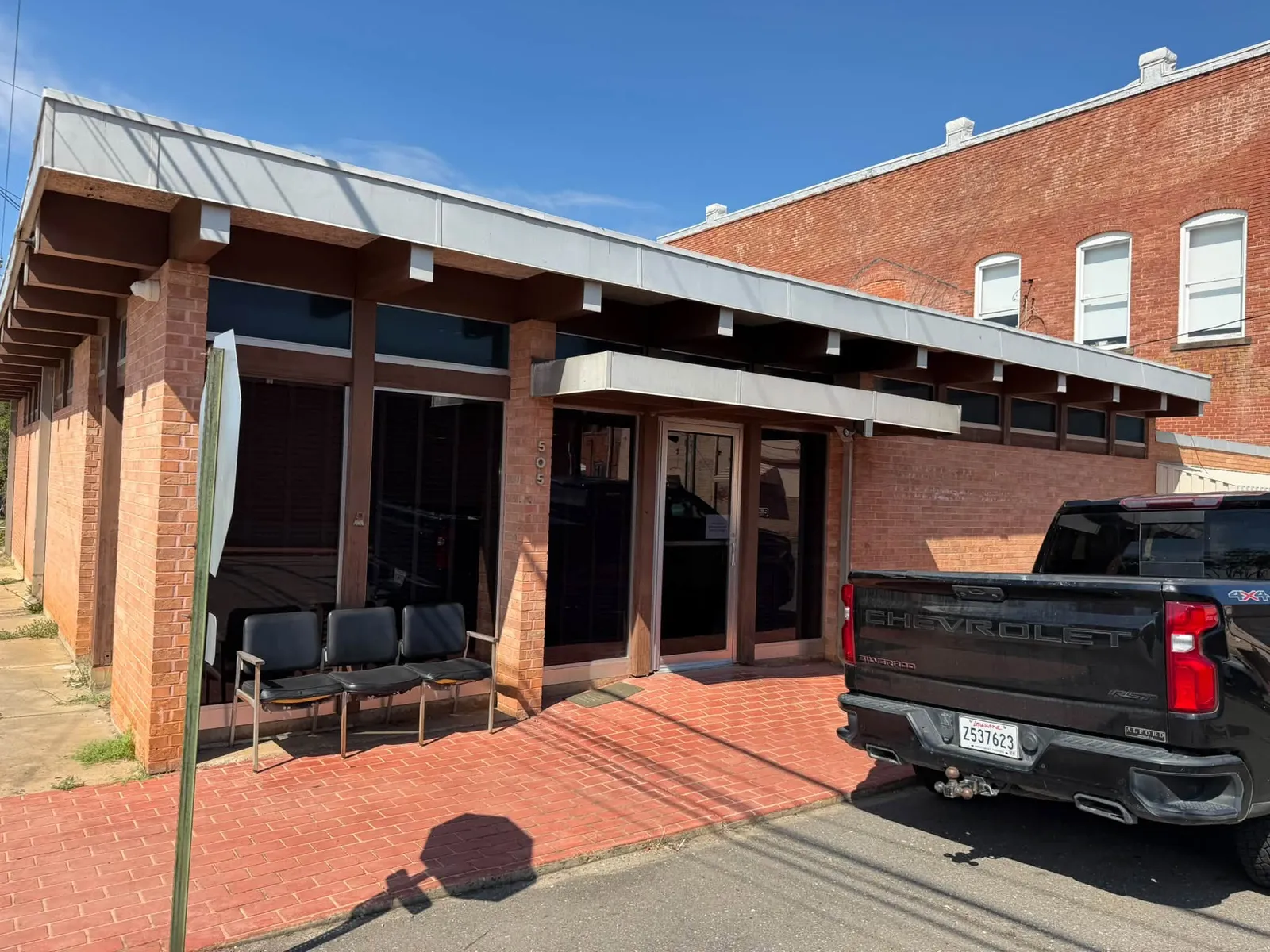 Entrance to a brick building with the number 505 beside the door and chairs along the wall.